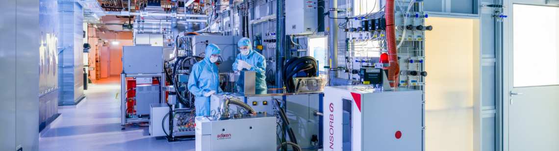 Man sieht Menschen in Laboranzügen in einem Reinraum mit vielen technischen Geräten.